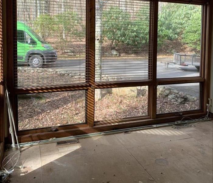 Carpet has been removed, only the subfloor remains. Big windows with the SERVPRO van outside. 