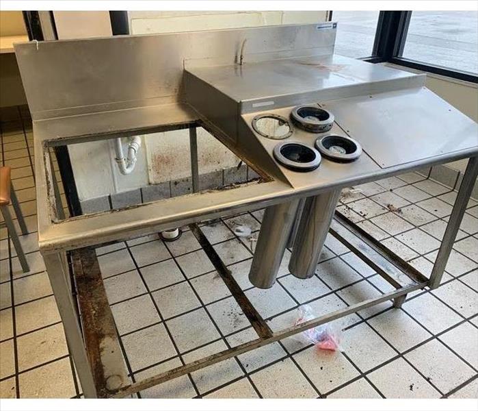 A metal table and tile floor are very dirty. Covered with black grease and dirt. 