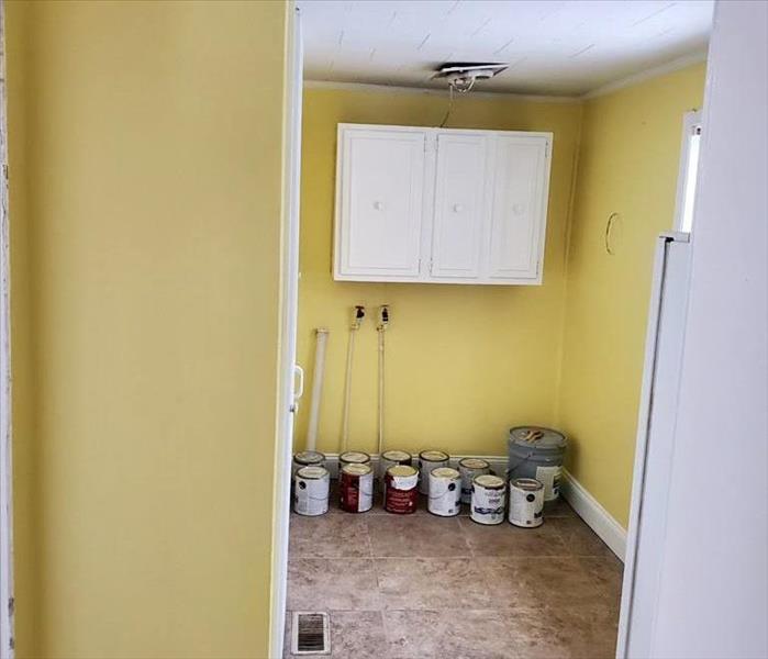 Same room with yellow walls and white ceiling. Paint cans are on floor against the wall. 