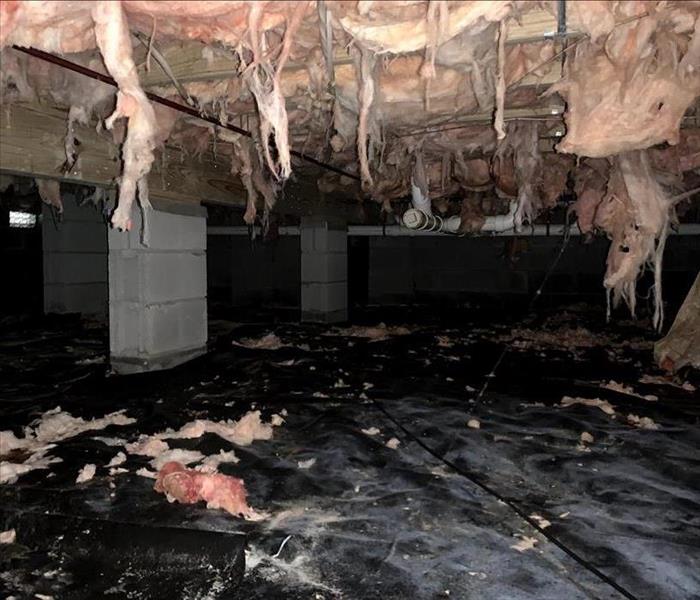A crawl space with pink insulation that is hanging down in places and a black vapor barrier