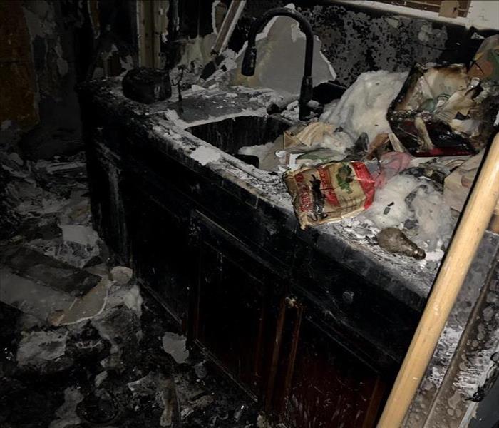 A bathroom sink is covered in black soot and debris caused by a fire. 