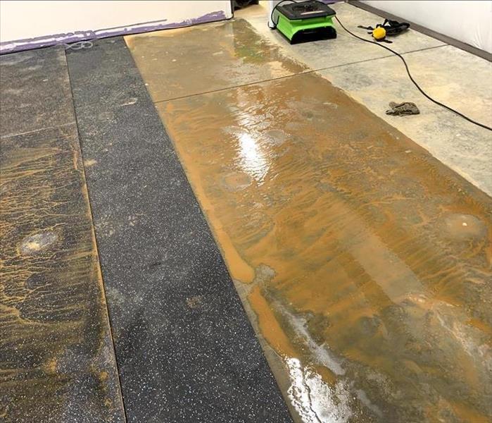 A concrete floor is wet and muddy. Dirty rubber mats have also been damaged on top of the concrete. 