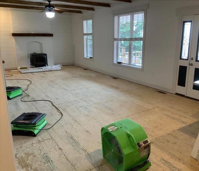 Open room with only the subfloor remaining and 3 SERVPRO air movers placed for drying. 