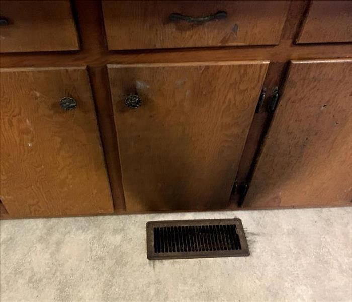 Black soot on wooden cabinets and surrounding a vent in the floor. 