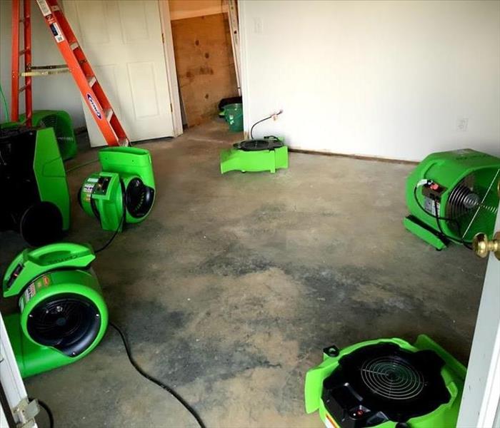 Concrete basement floor is dry with 4 green SERVPRO air movers placed in it.